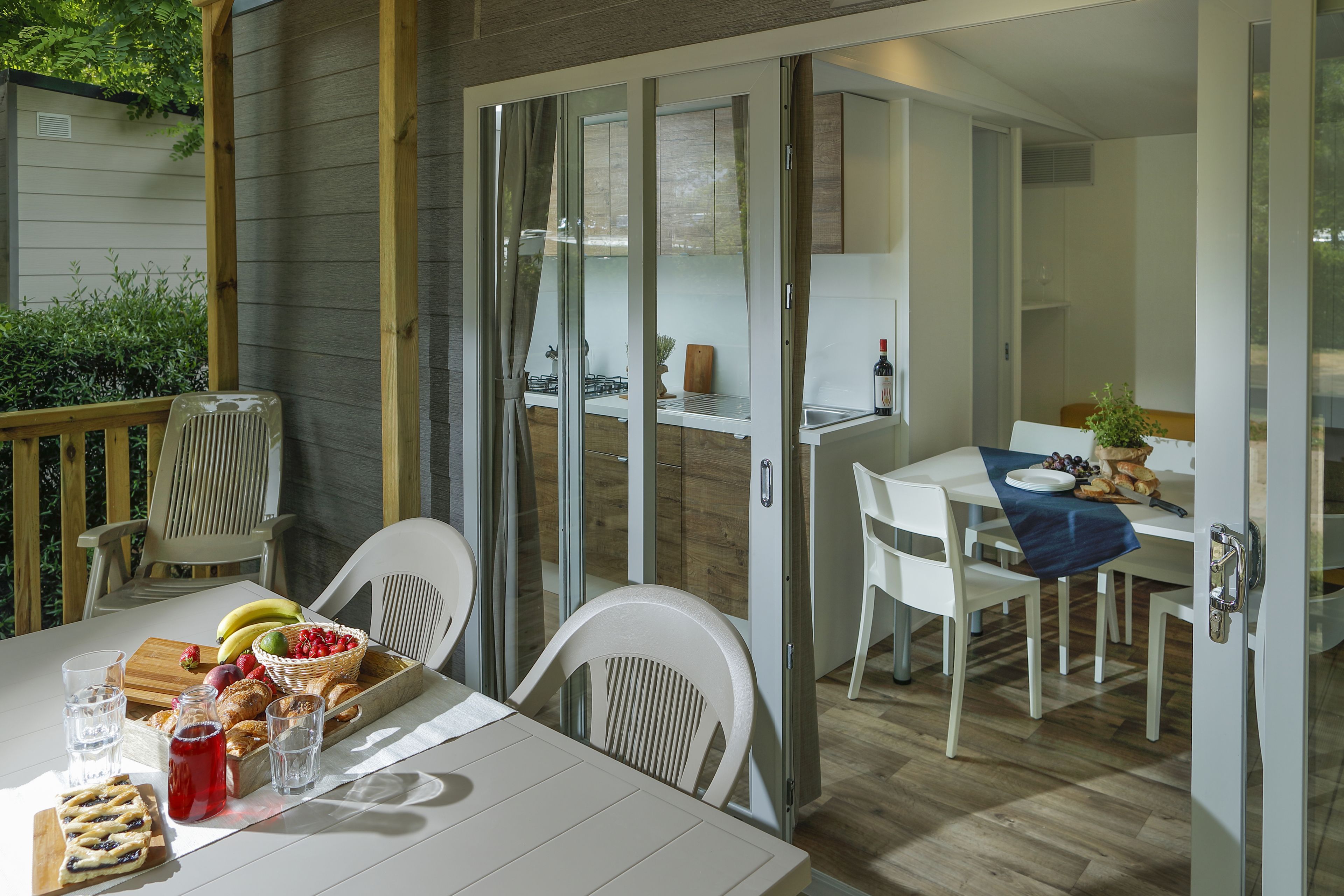A dining area with a table set for two, a basket of fruit, and a bottle of wine.