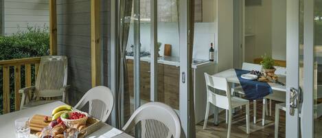 Un comedor con una mesa lista para dos personas, una cesta de fruta y una botella de vino.