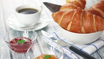 Une table avec des croissants, une tasse de café et deux petits pots de confiture.