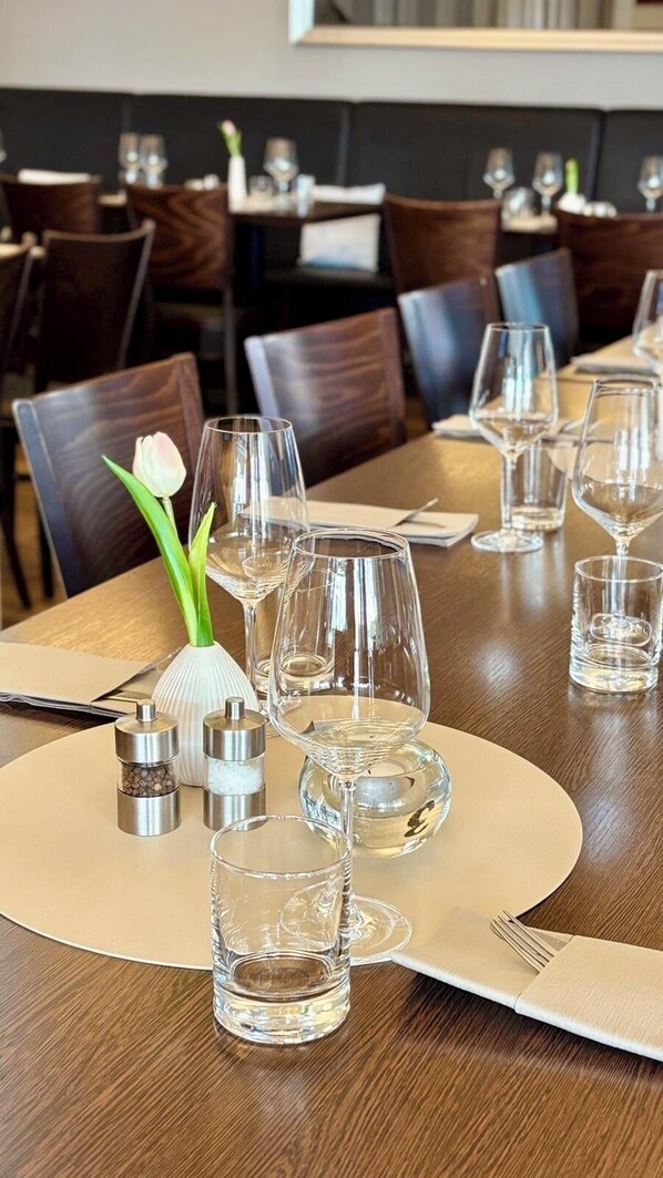 A dining table set with clear glasses, a vase with a single flower, salt and pepper shakers, and a folded napkin. - Bodensee Yachthotel Schattmaier (Kressbronn)