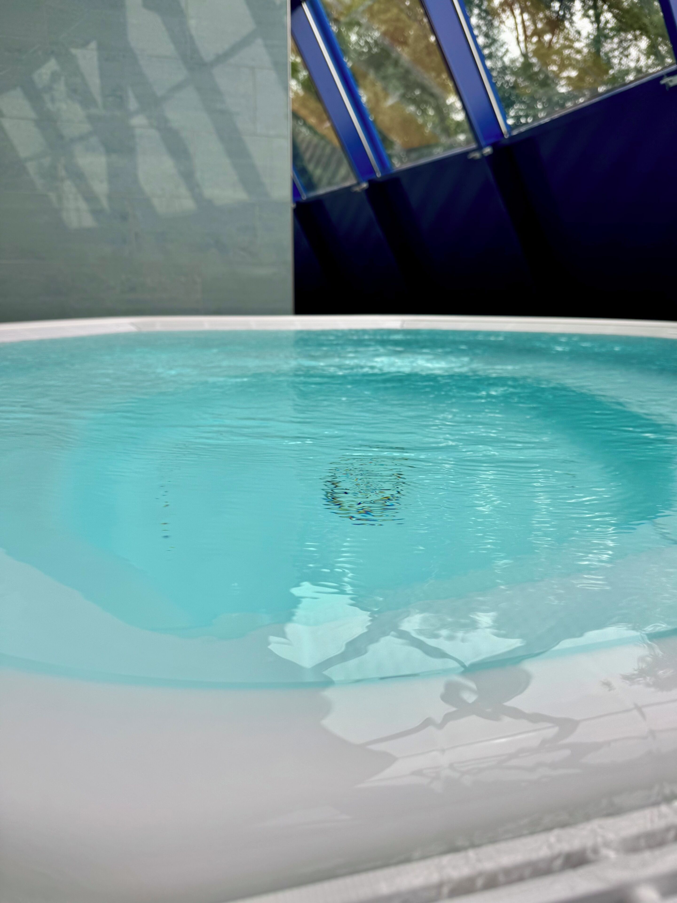 A pool with clear water, a tiled edge, and a blue structure in the background.