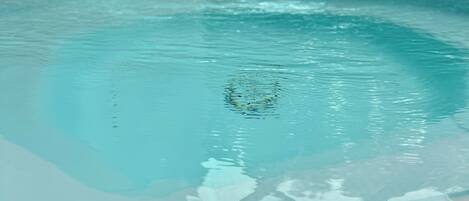 A pool with clear water, a tiled edge, and a blue structure in the background.