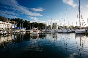 A marina with multiple sailboats docked, a building with a blue awning, and calm water reflecting the boats. - Bodensee Yachthotel Schattmaier (Kressbronn)