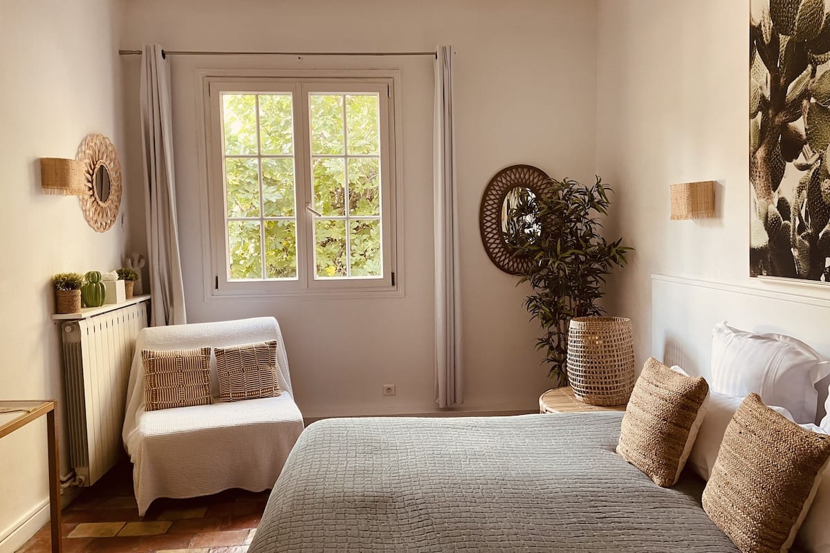 Une chambre avec un grand lit, deux tables de chevet, une chaise, un radiateur, une fenêtre avec des rideaux et un miroir fixé au mur.