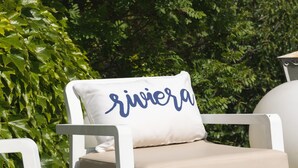 Un fauteuil de jardin blanc, doté d’un coussin beige et d’un oreiller sur lequel est inscrit le mot « rivier ».