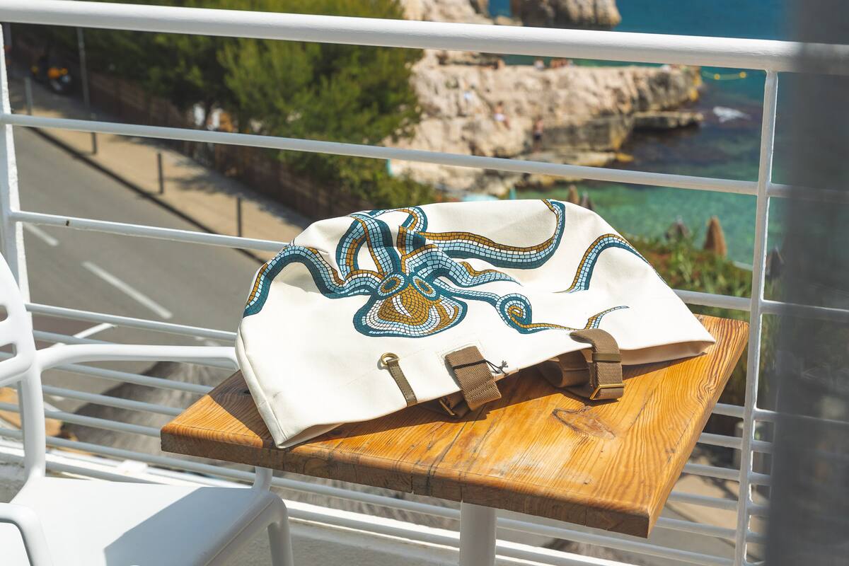 Un balcon avec une table et des chaises, donnant sur une zone côtière aux eaux d’un bleu limpide et aux falaises rocheuses.