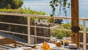Une terrasse avec une table dressée pour le dîner, offrant une vue sur une étendue d’eau et un paysage rocheux.