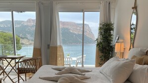 Een slaapkamer met een groot bed, uitzicht op zee en een eethoek met een tafel en stoelen.