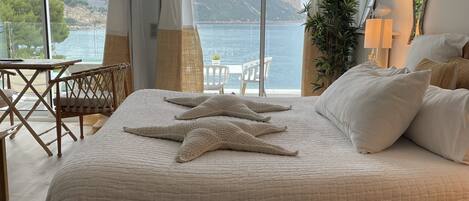 A bedroom with a large bed, a view of the sea, and a dining area with a table and chairs.
