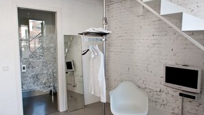 A modern room with a white brick wall, a white chair, a coat rack with clothes, a TV, and a staircase. - Legrenzi Rooms (Mestre)