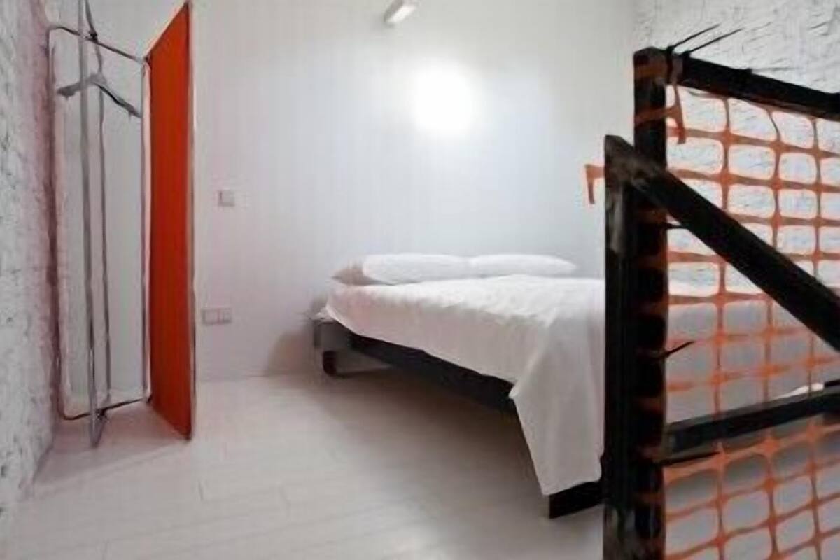 Ein kleines, schlichtes Zimmer mit einem Bett, einer weißen Wand und einer Tür.