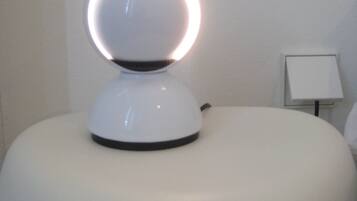 Un objet blanc, rond et lumineux, posé sur une surface blanche, qui pourrait être une lampe, avec un petit objet blanc et rectangulaire à sa droite.