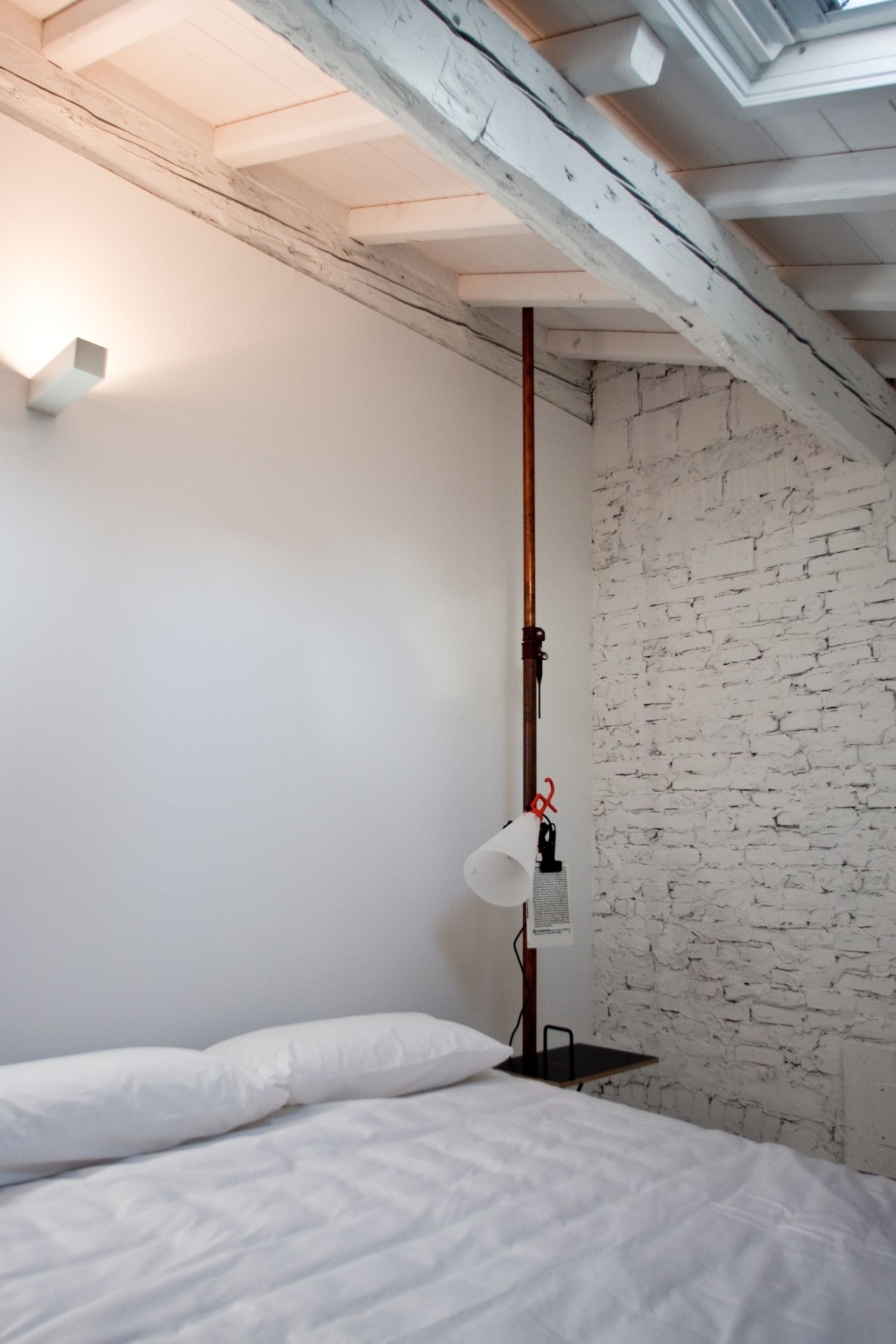A bedroom with a bed, white walls, a brick wall, and a skylight.