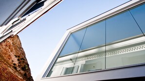 A modern building with a large glass window reflecting the sky and a brick wall. - Legrenzi Rooms (Mestre)