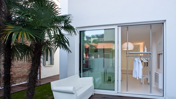 A modern outdoor area with a white sofa, a glass door leading to a room with a bathroom and a drying rack. - Legrenzi Rooms (Mestre)