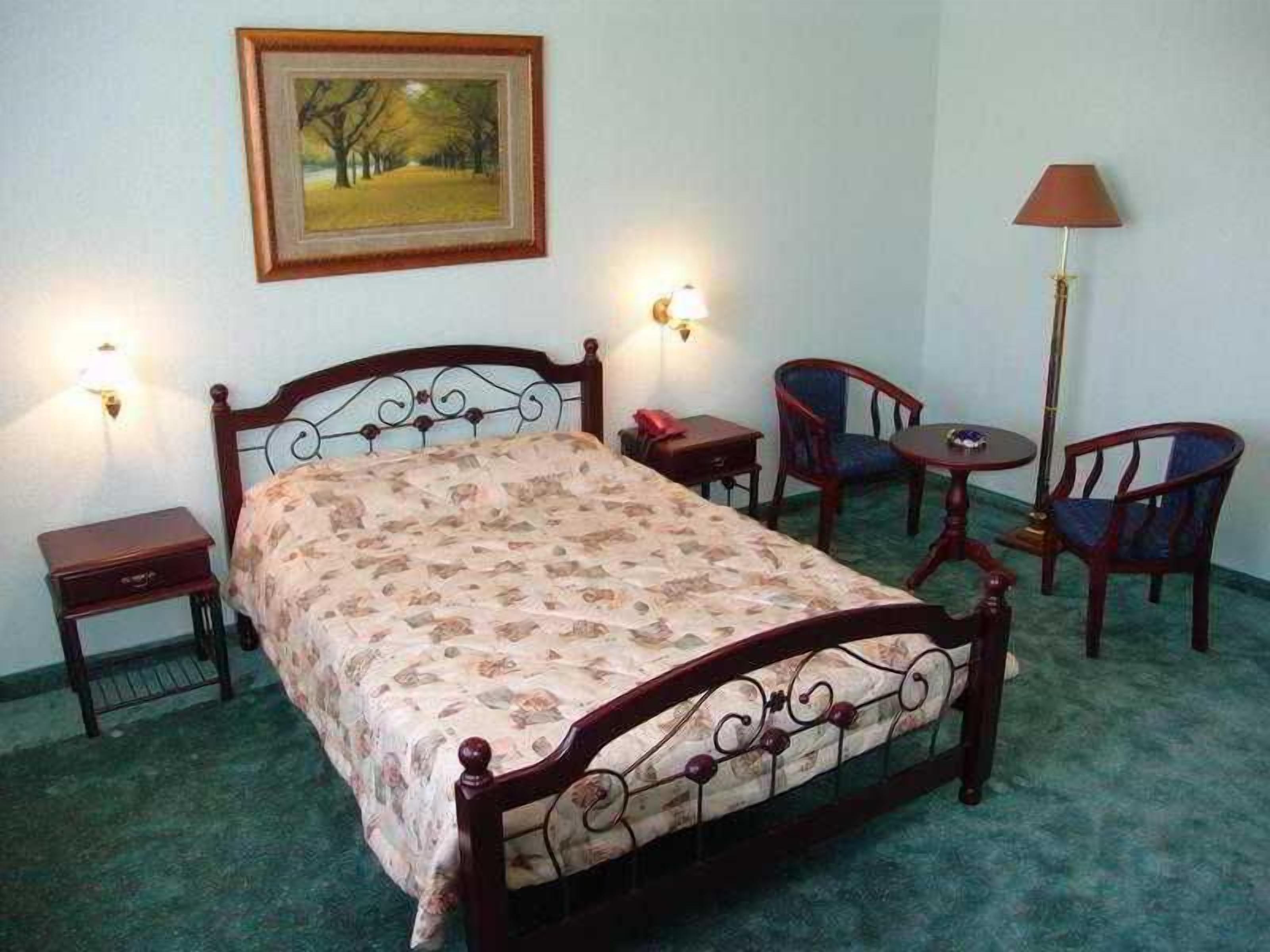 A bedroom with a bed, bedside tables, a chair, a small table, and a lamp.