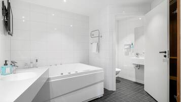 Un bagno moderno con una vasca da bagno ampia, un lavandino separato e un WC.