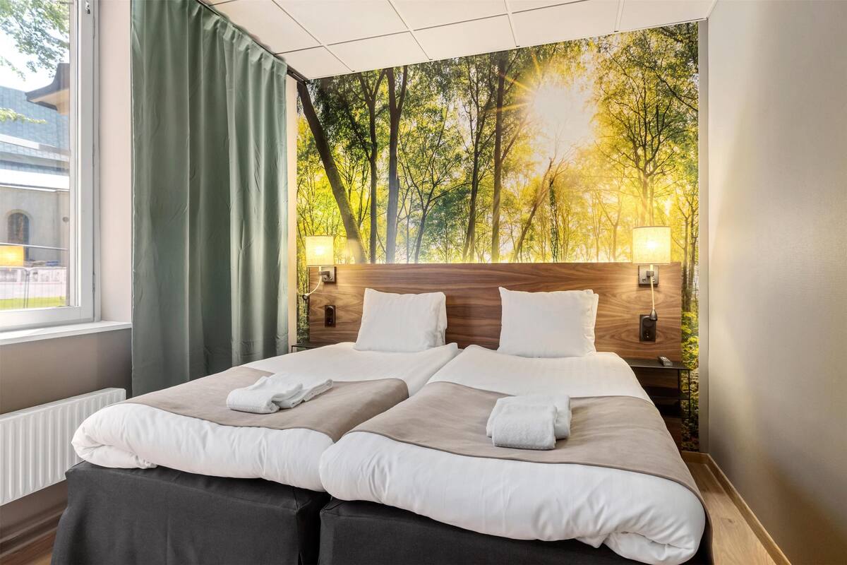 Habitación doble con dos camas, un ventanal grande y un mural temático de bosque.