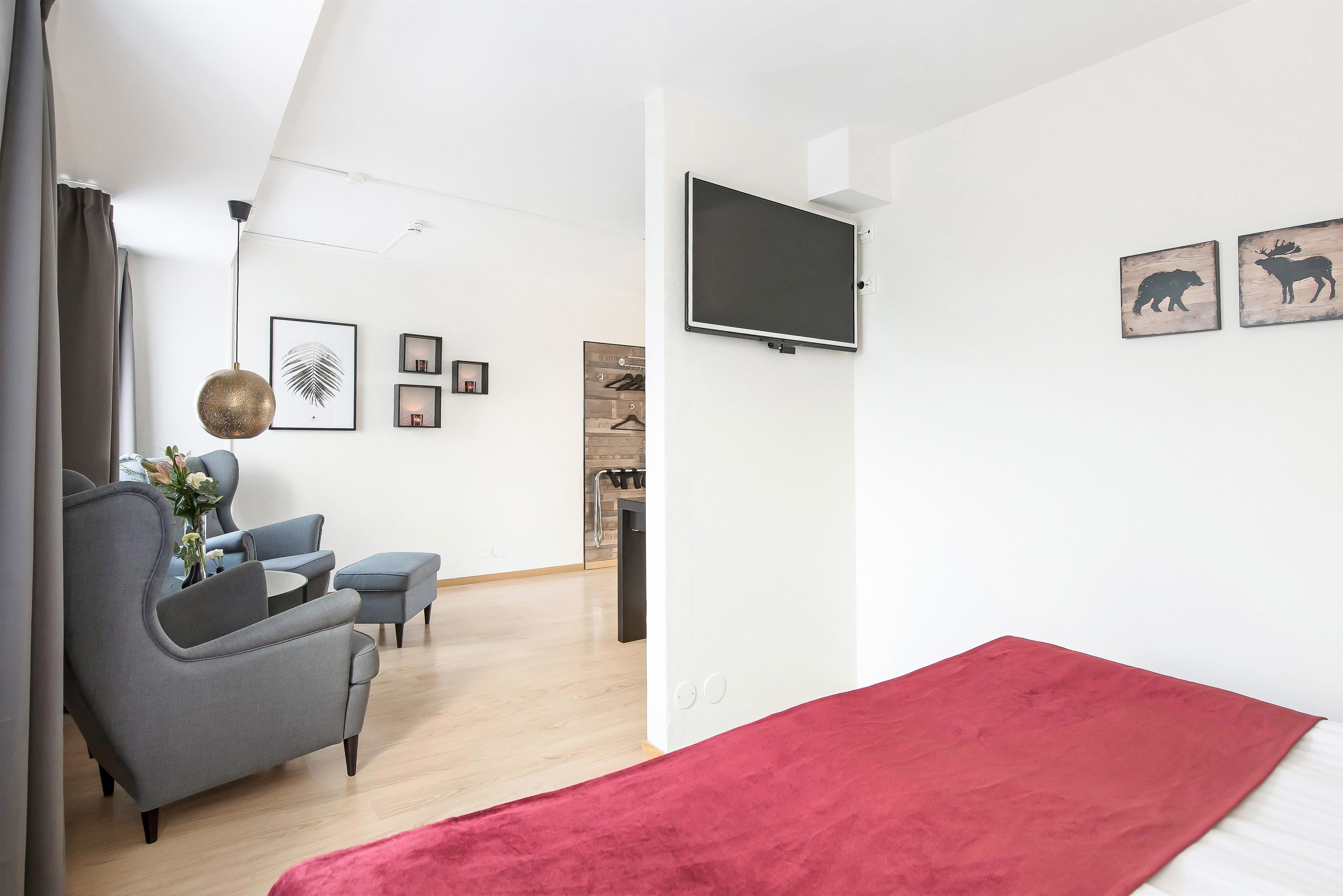 A modern living room with a grey sofa, a red rug, and a flat-screen TV mounted on the wall.