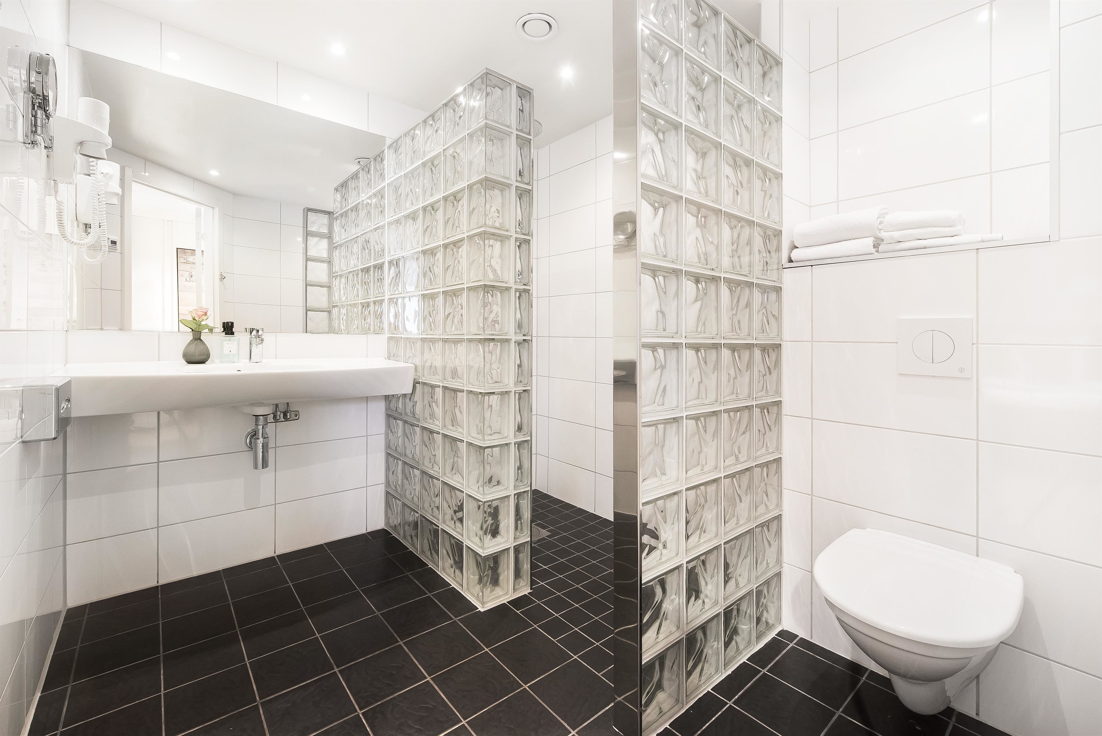 Un baño moderno con un lavabo blanco, piso de baldosas negras y cabina de ducha de vidrio.