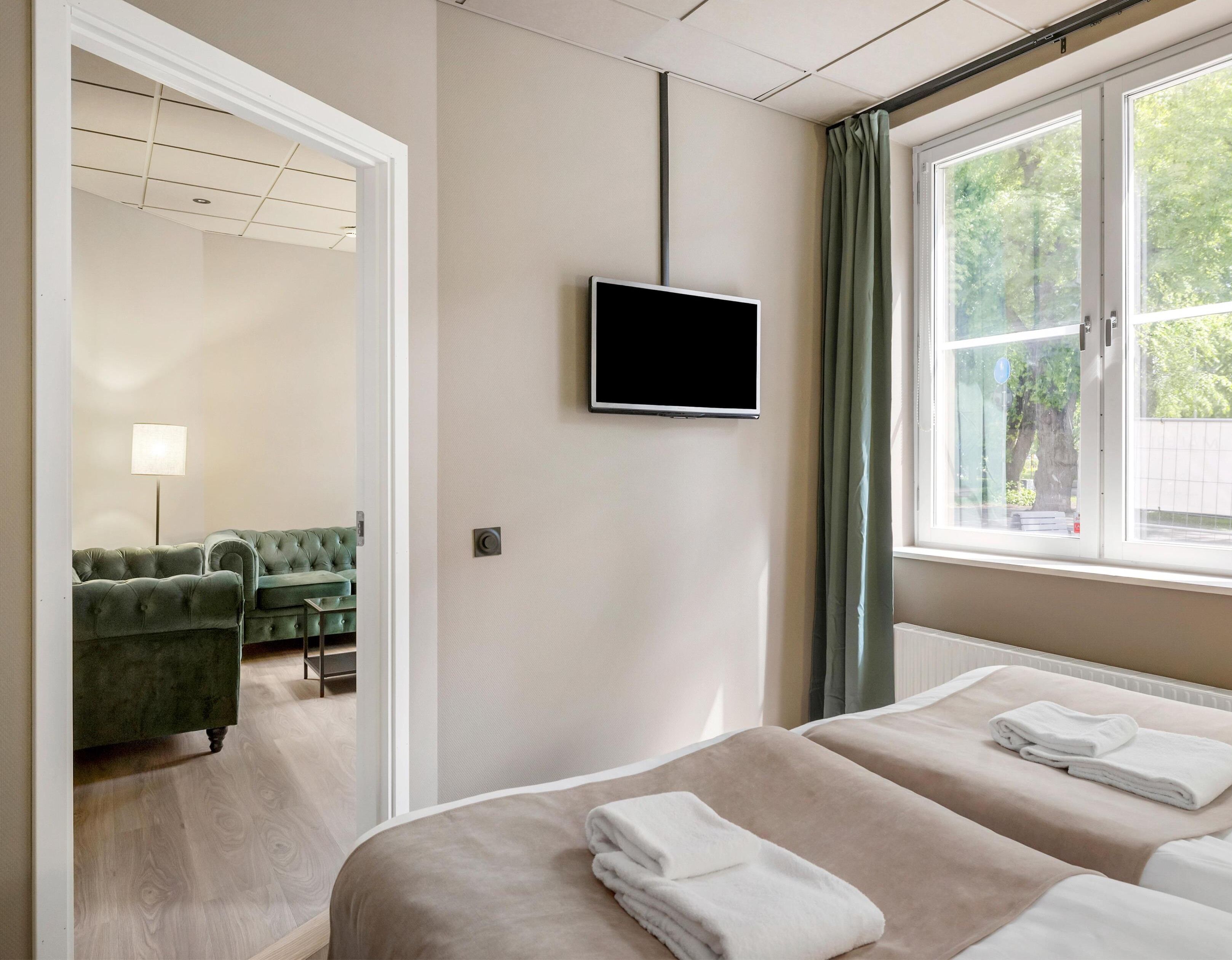 Ett hotellrum med två sängar, en tv, en grön soffa och ett fönster med gardiner.