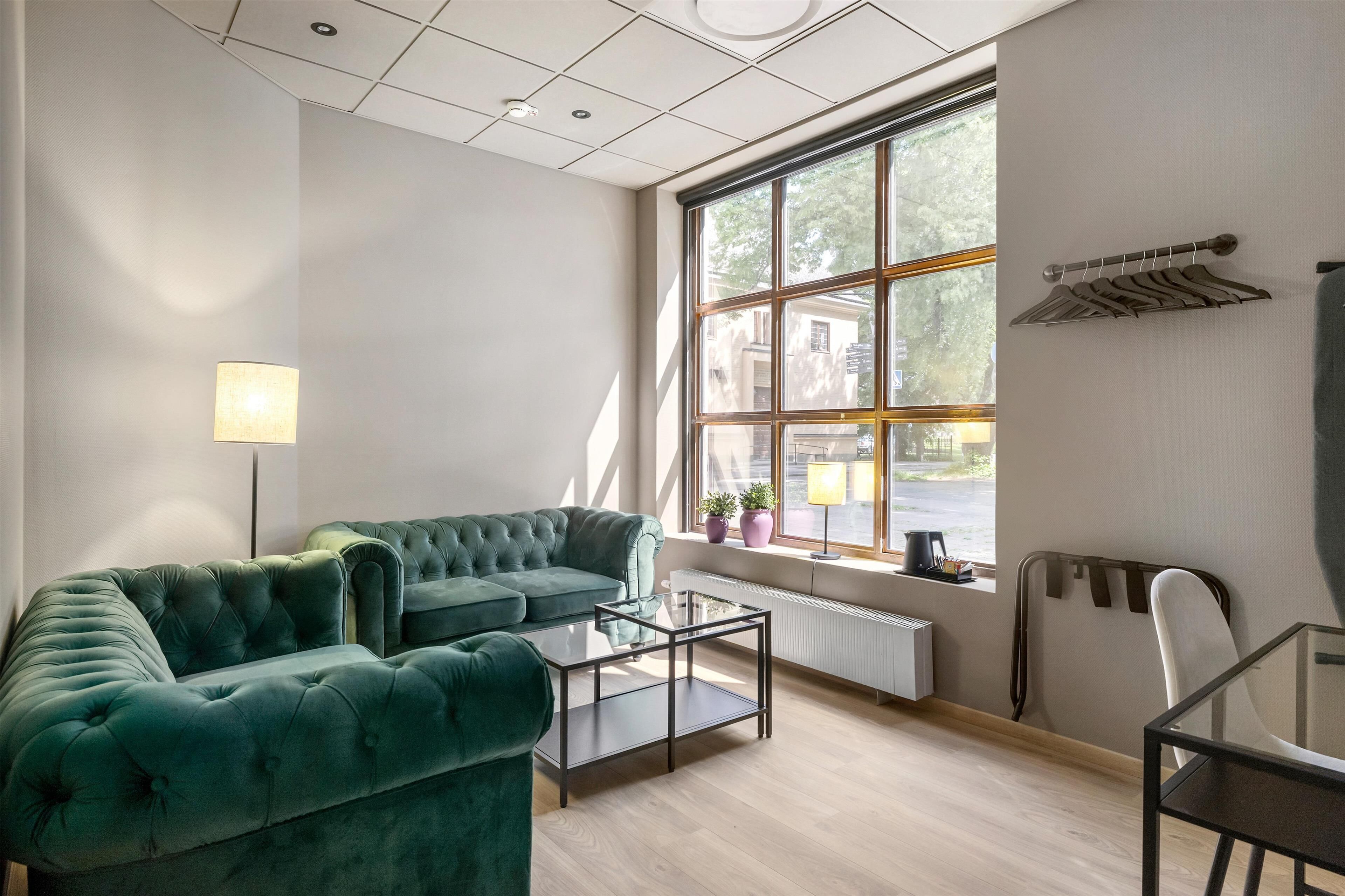 Una sala de estar moderna con un sofá verde, una mesa de centro de vidrio y vistas a la calle a través de ventanas amplias.