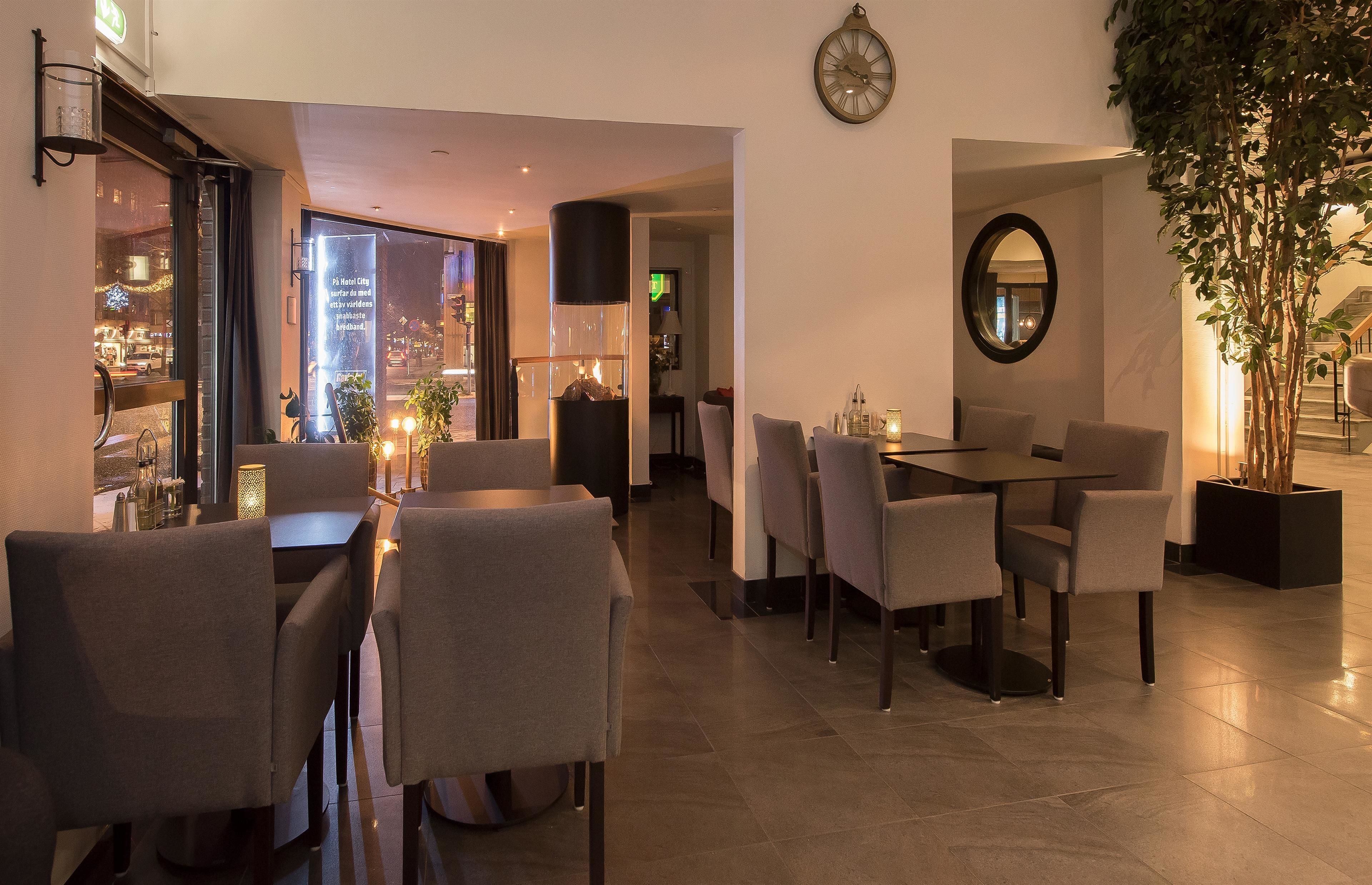 A modern dining area with a large table and chairs, a clock on the wall, and a view of the city at night.