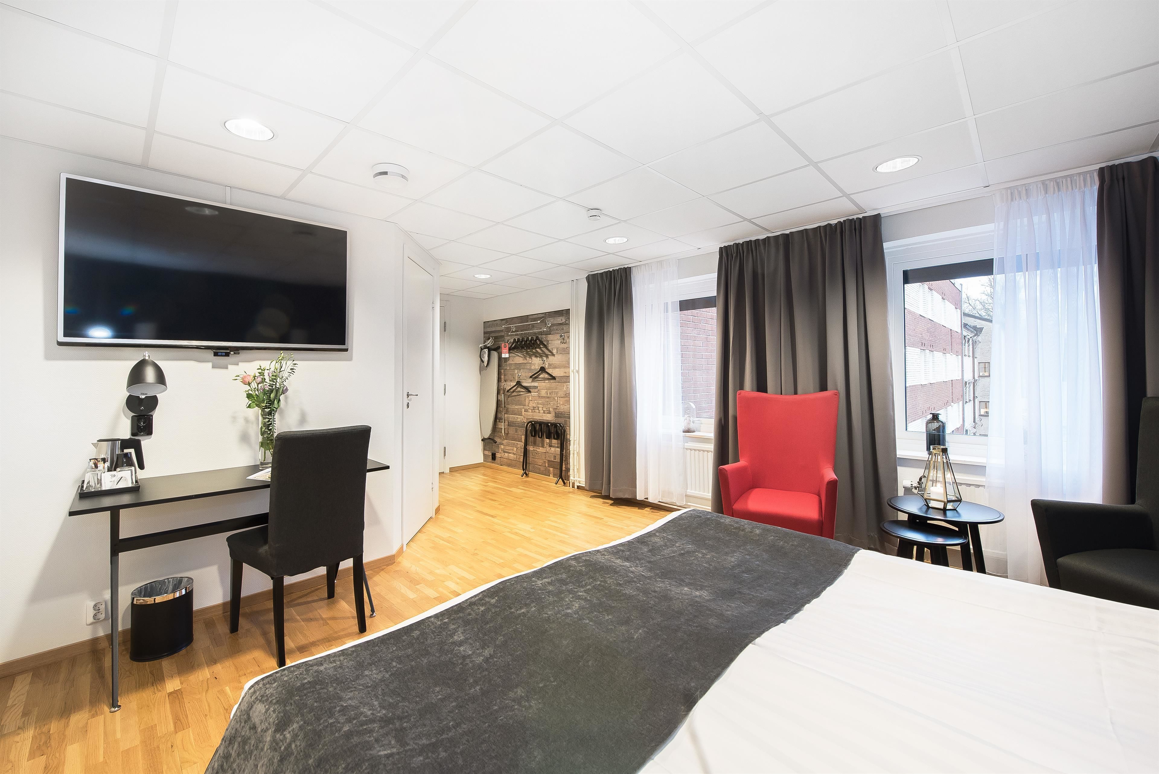 Una habitación de hotel con una cama, un escritorio con una silla, un televisor y un sillón rojo.