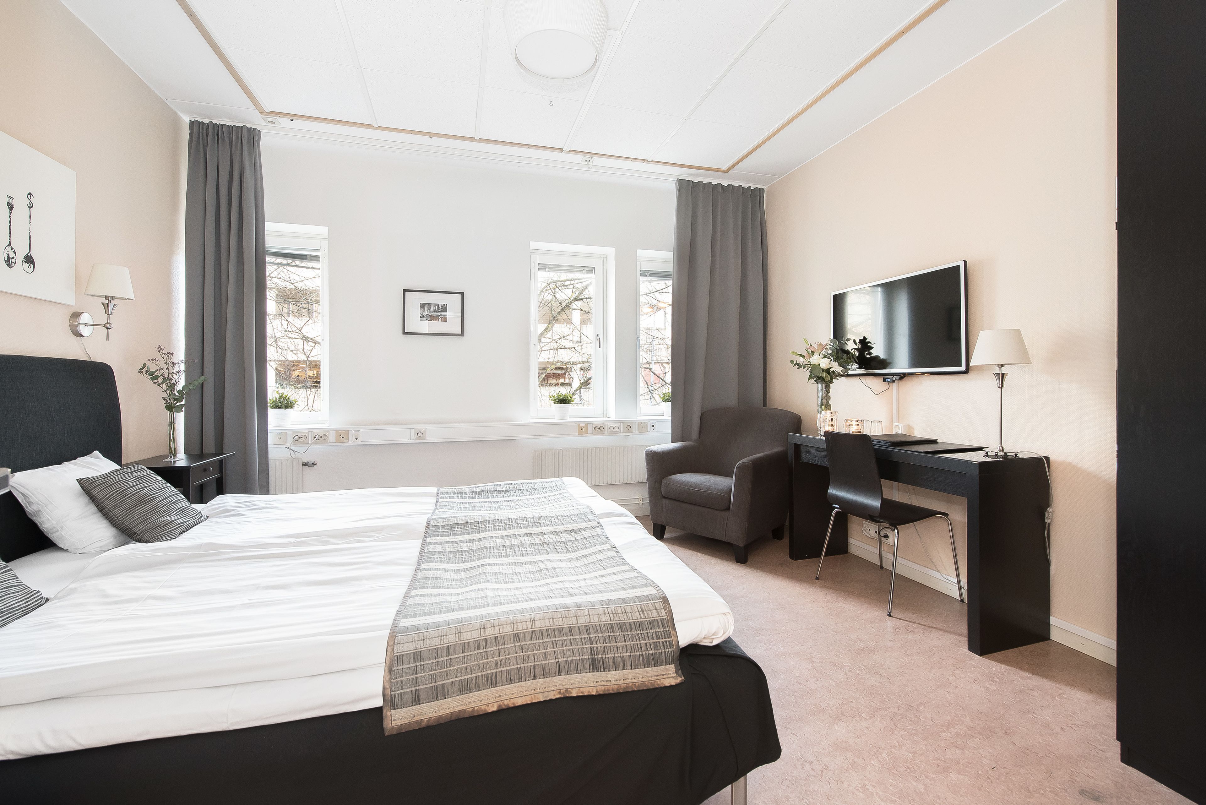 A hotel room with a bed, a desk, a chair, a TV, and a window with curtains.