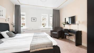 A hotel room with a bed, a desk, a chair, a TV, and a window with curtains.