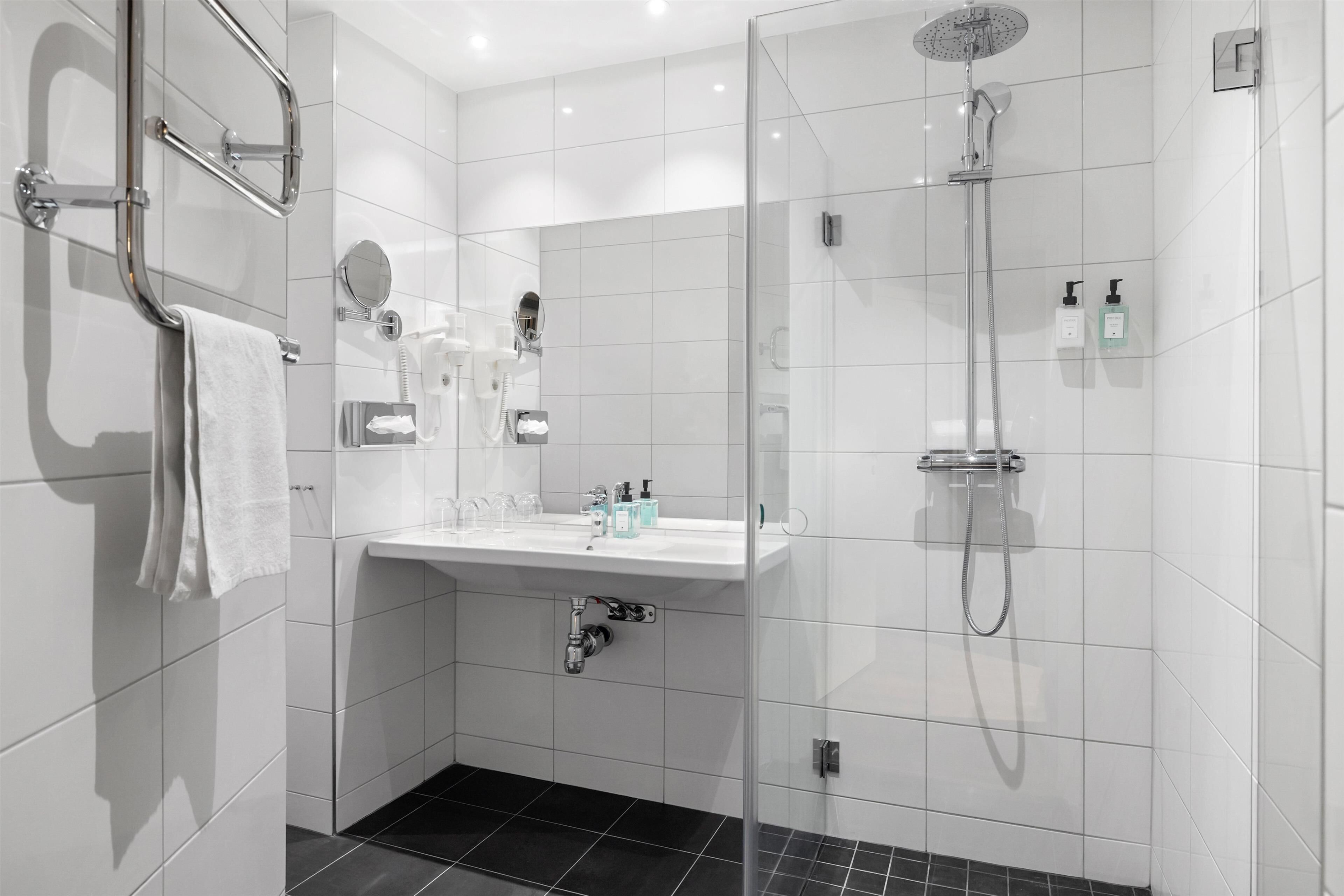 A modern bathroom with a glass shower enclosure, a white sink, and a towel rack.