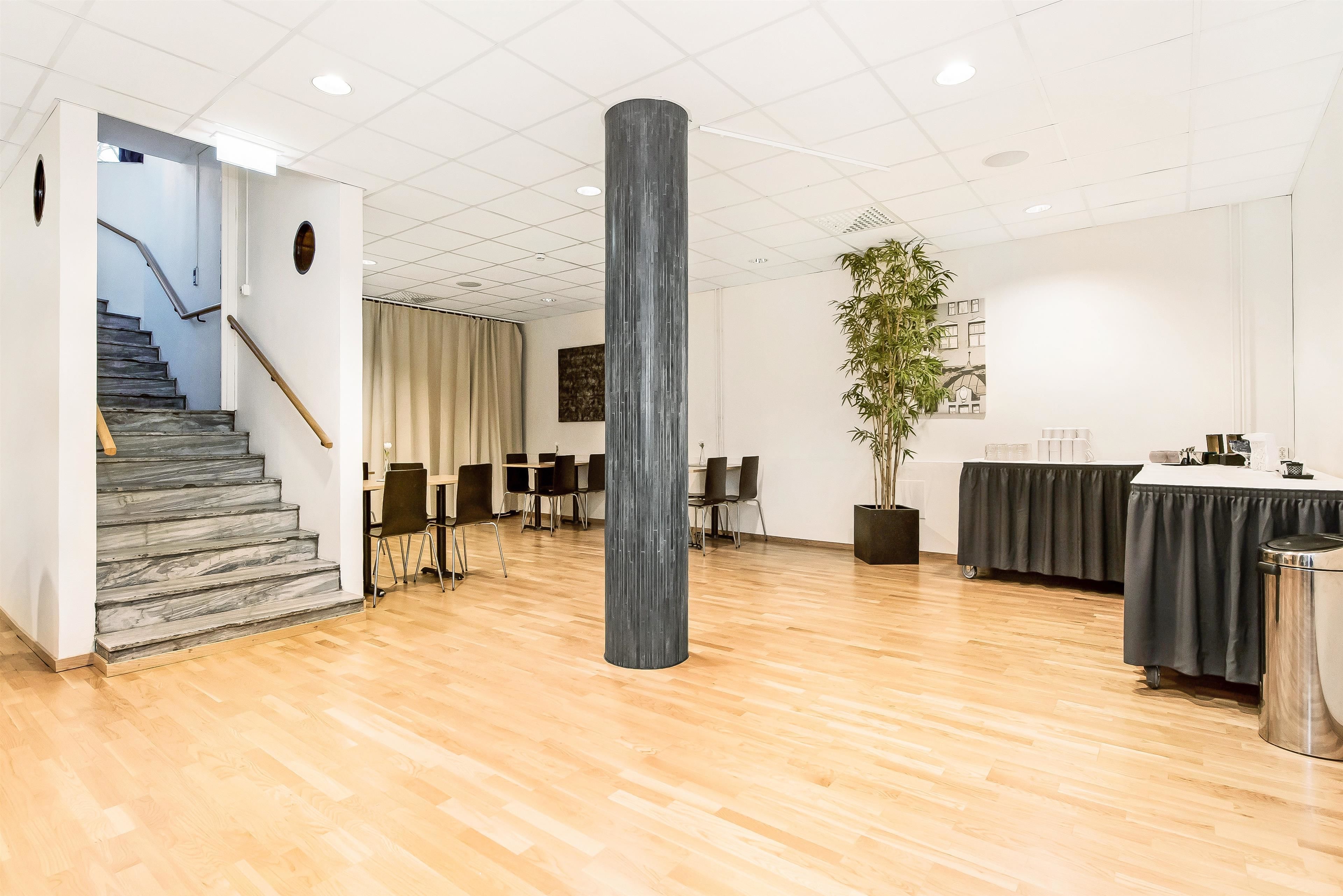A spacious lobby with a staircase, a large pillar, a reception desk, and a potted plant.