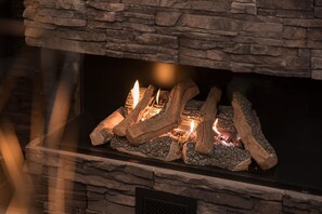 Ein Kamin mit Holzscheiten und Flammen, eingebaut in eine Steinwand.
