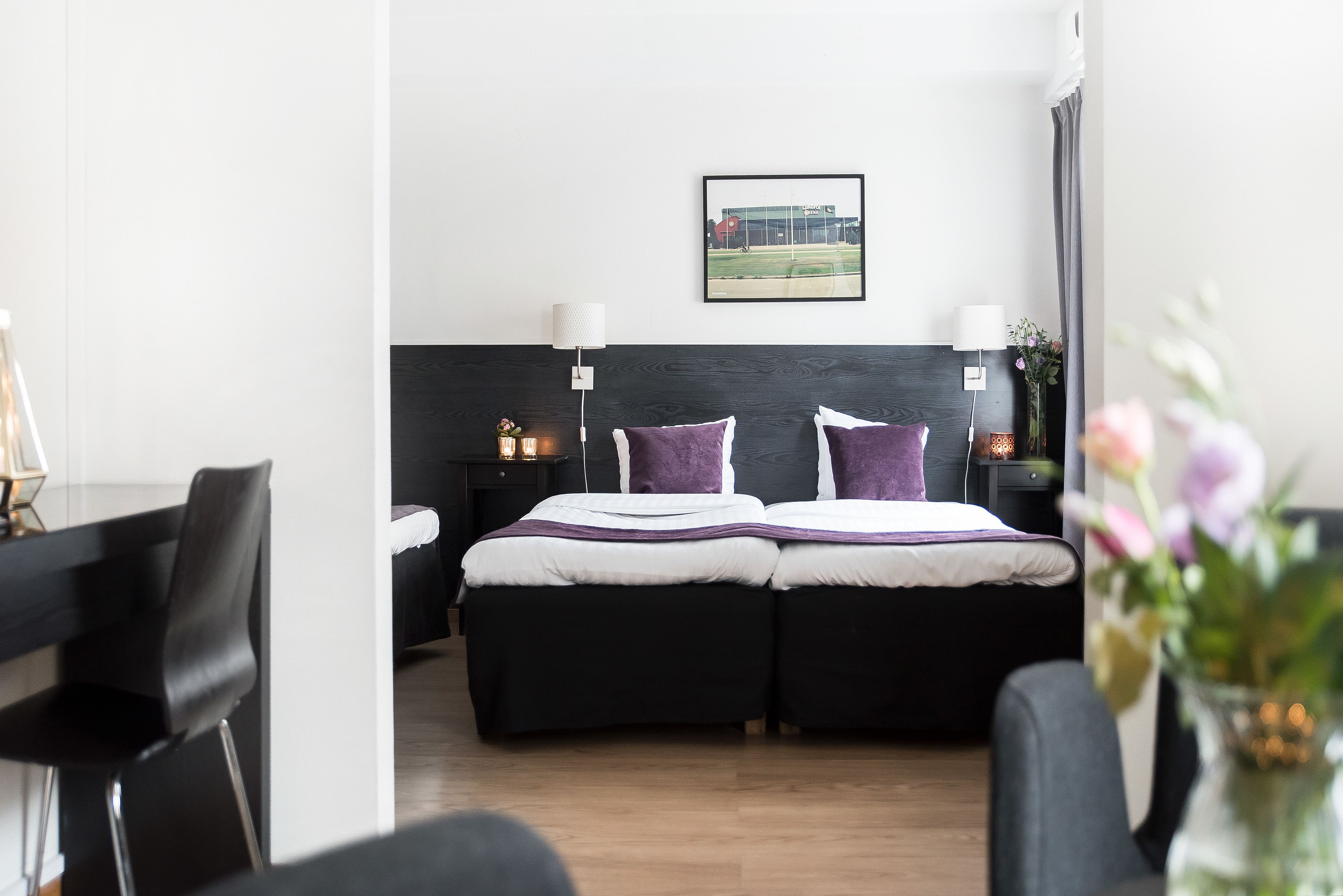 A modern hotel room with a bed, bedside tables, a lamp, and a framed picture on the wall.