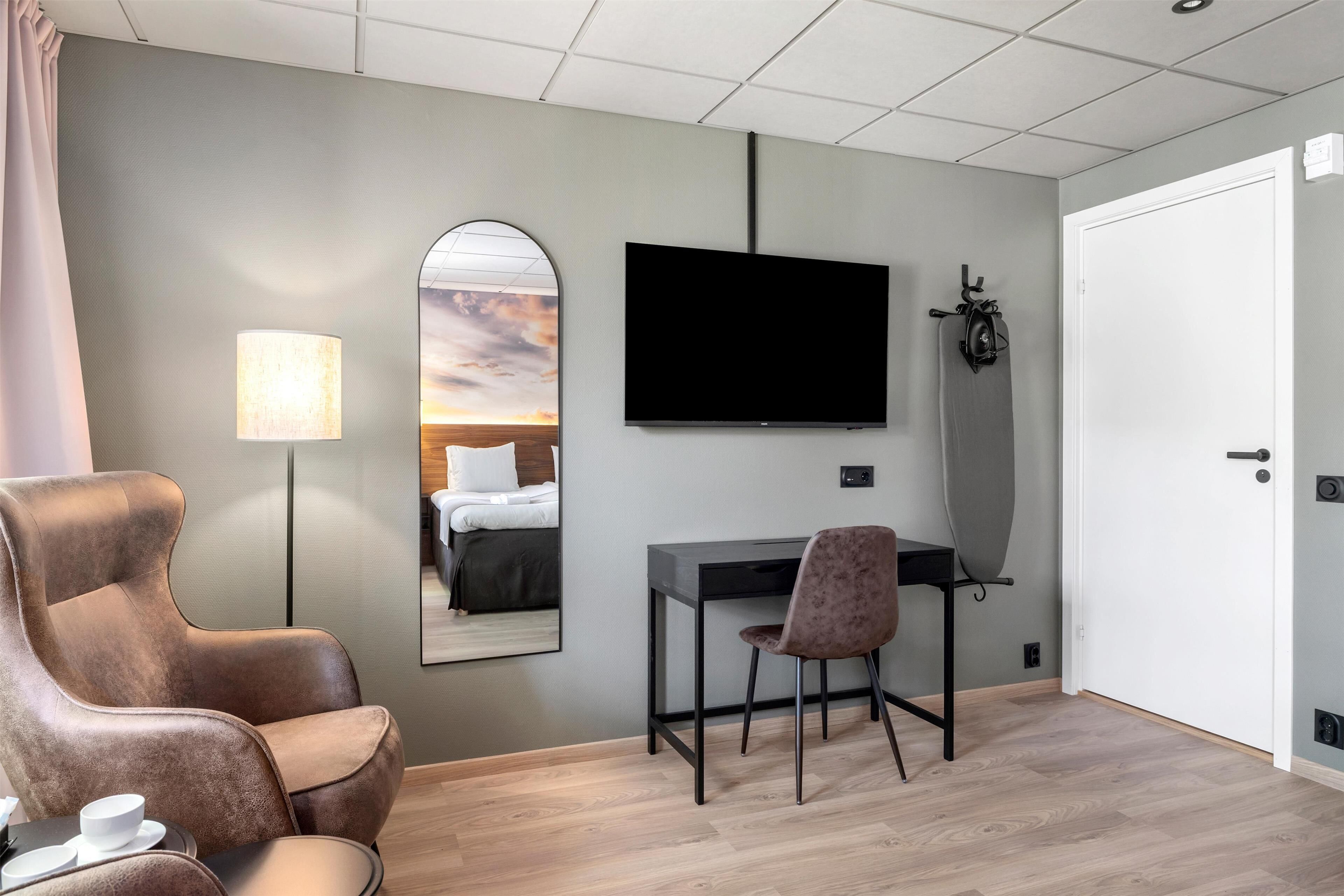 Une chambre d’hôtel moderne équipée d’un grand lit, d’un bureau avec une chaise, d’une télévision et d’un miroir.
