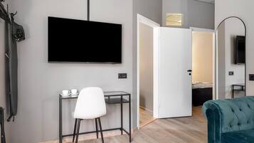 Une chambre d’hôtel moderne équipée d’un téléviseur à écran plat fixé au mur, d’un petit bureau avec une chaise, d’un canapé de couleur turquoise et d’une porte donnant sur une autre pièce.
