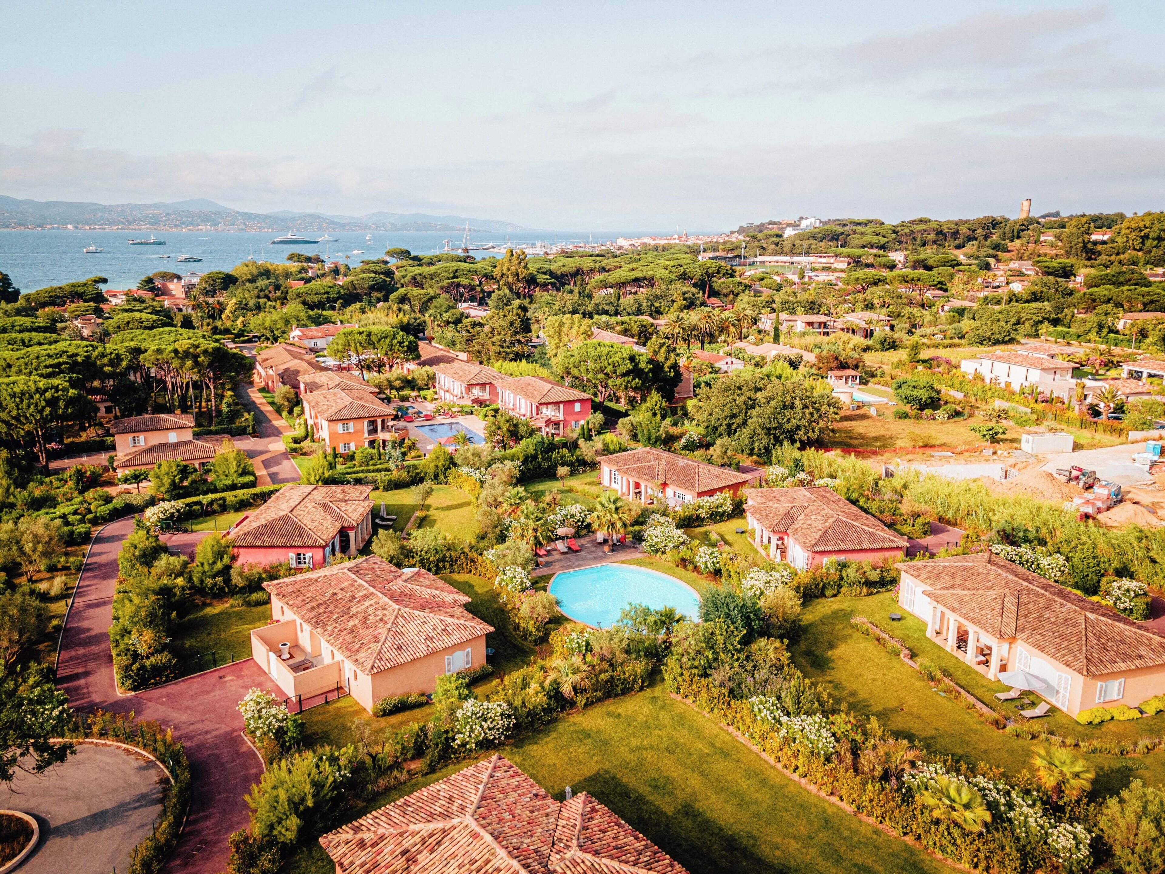 An aerial view of a residential area with houses, a swimming pool, and a view of the sea.