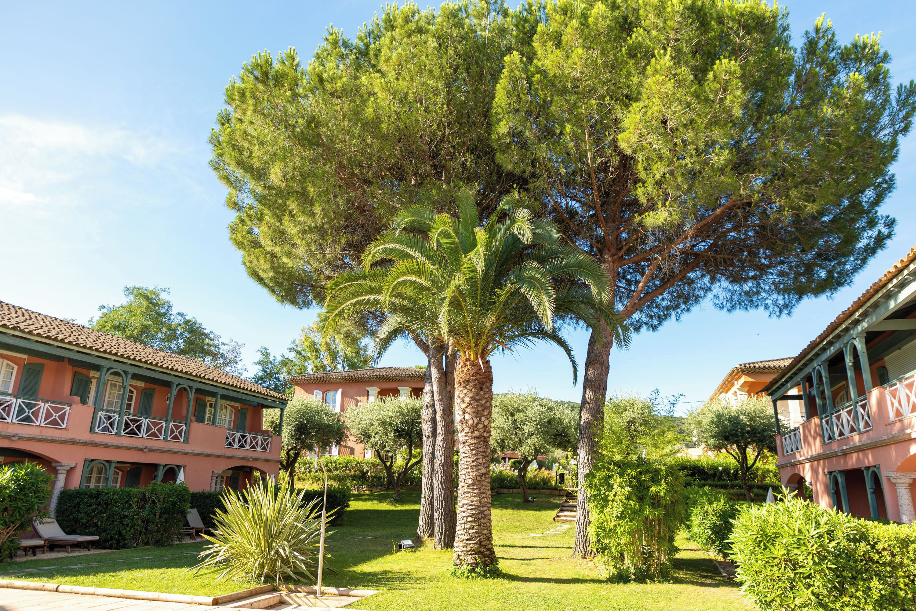 A two-story building with a garden, palm trees, and a clear blue sky.