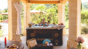 Estructura de piedra con un jacuzzi, una mesa con un plato de comida y un banco con un ventilador y zapatillas.
