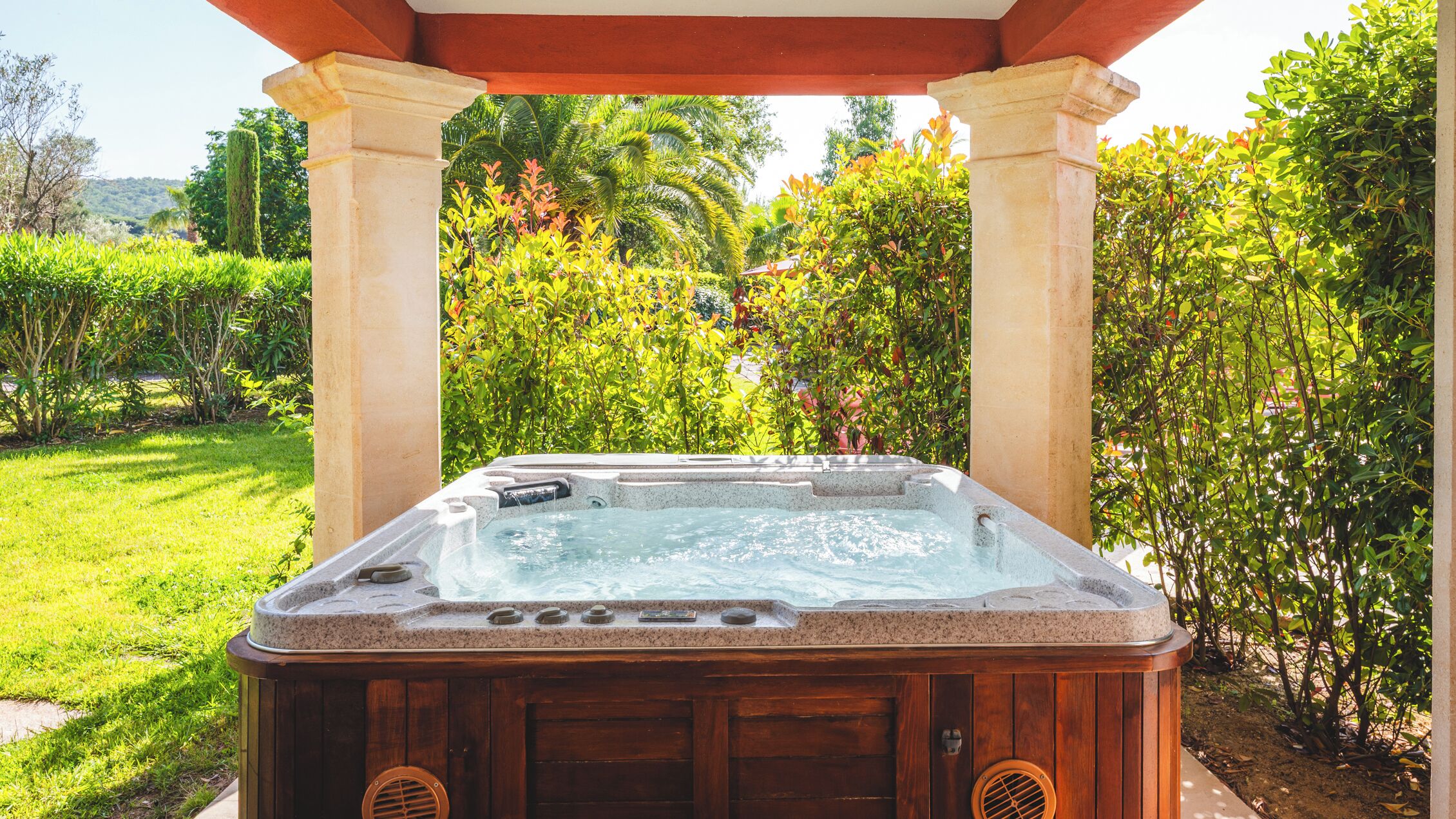 A hot tub under a pergola with a garden view.