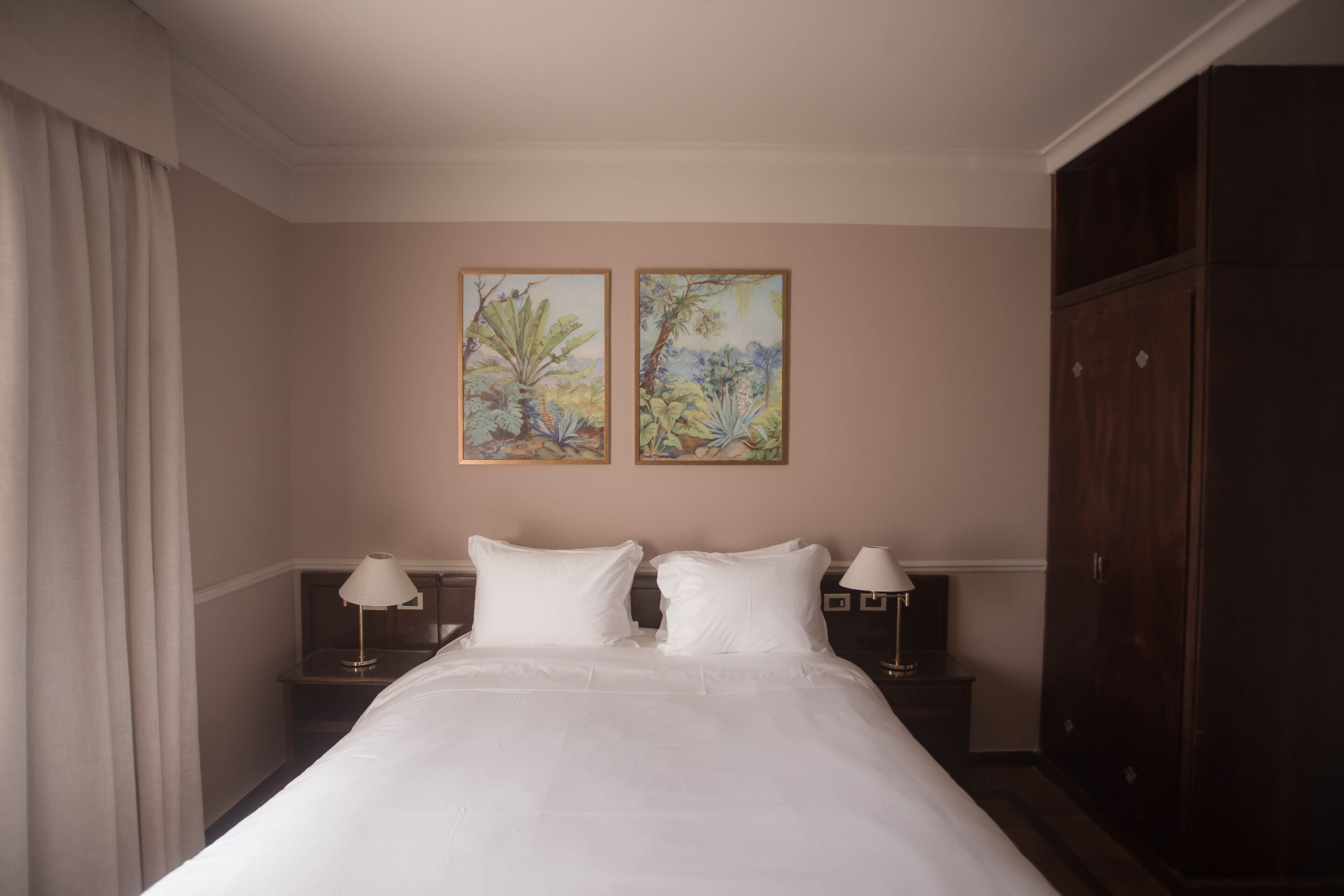 Una habitación de hotel con una cama grande, dos mesitas de noche, un armario y dos cuadros colgados en la pared.