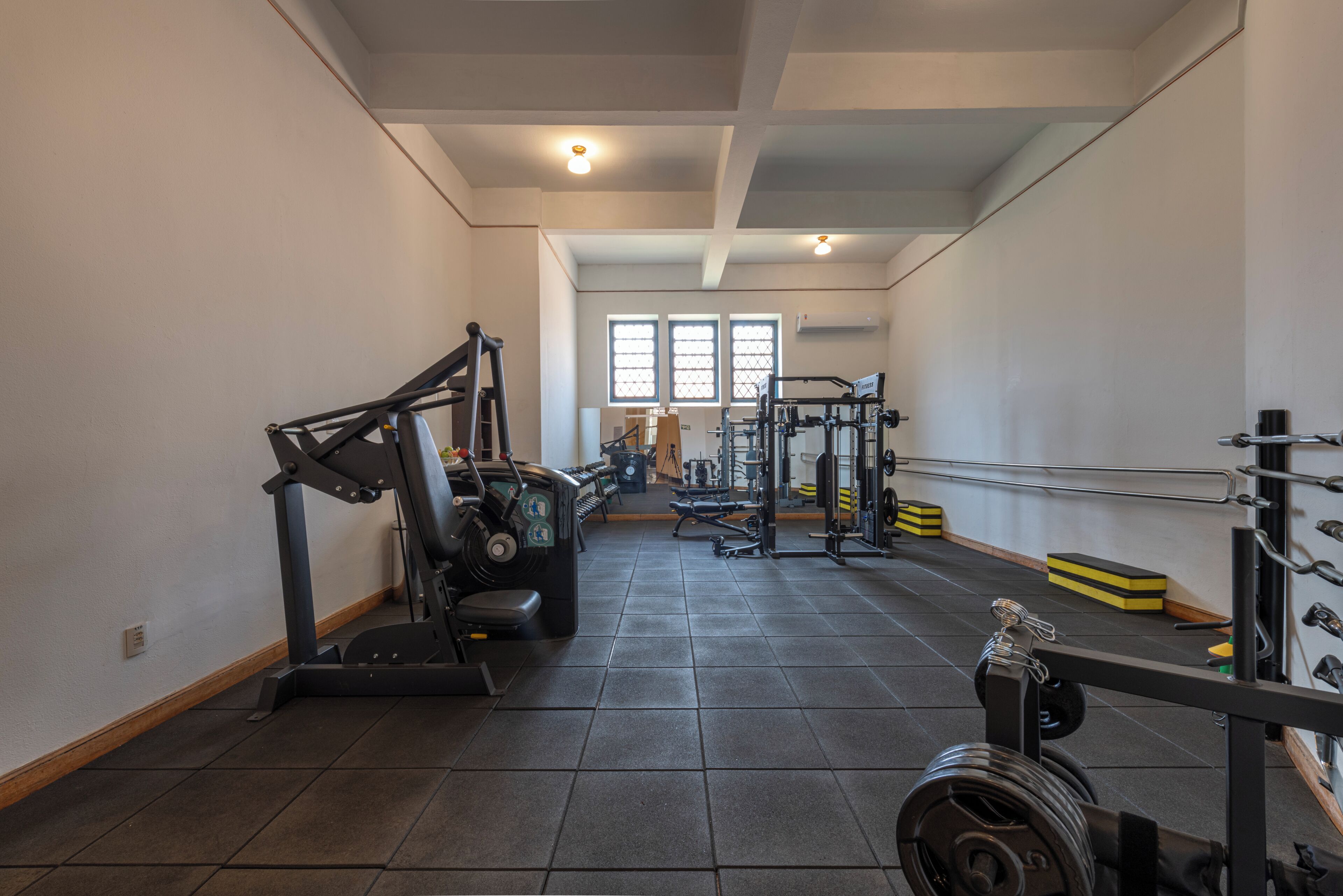 A gym with exercise equipment, a weight rack, and a window providing natural light.
