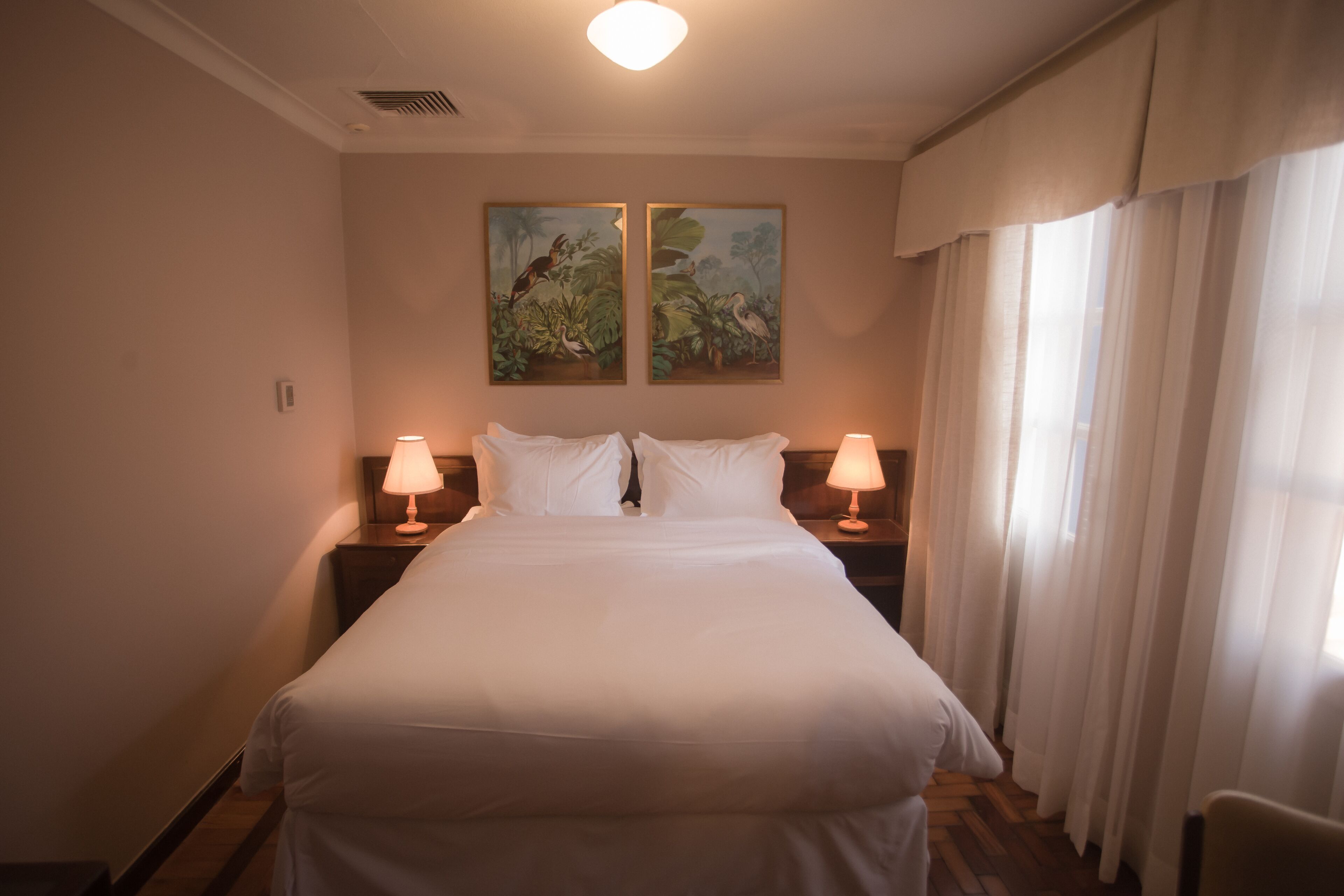A hotel room with a large bed, two bedside tables with lamps, and two wall-mounted paintings.