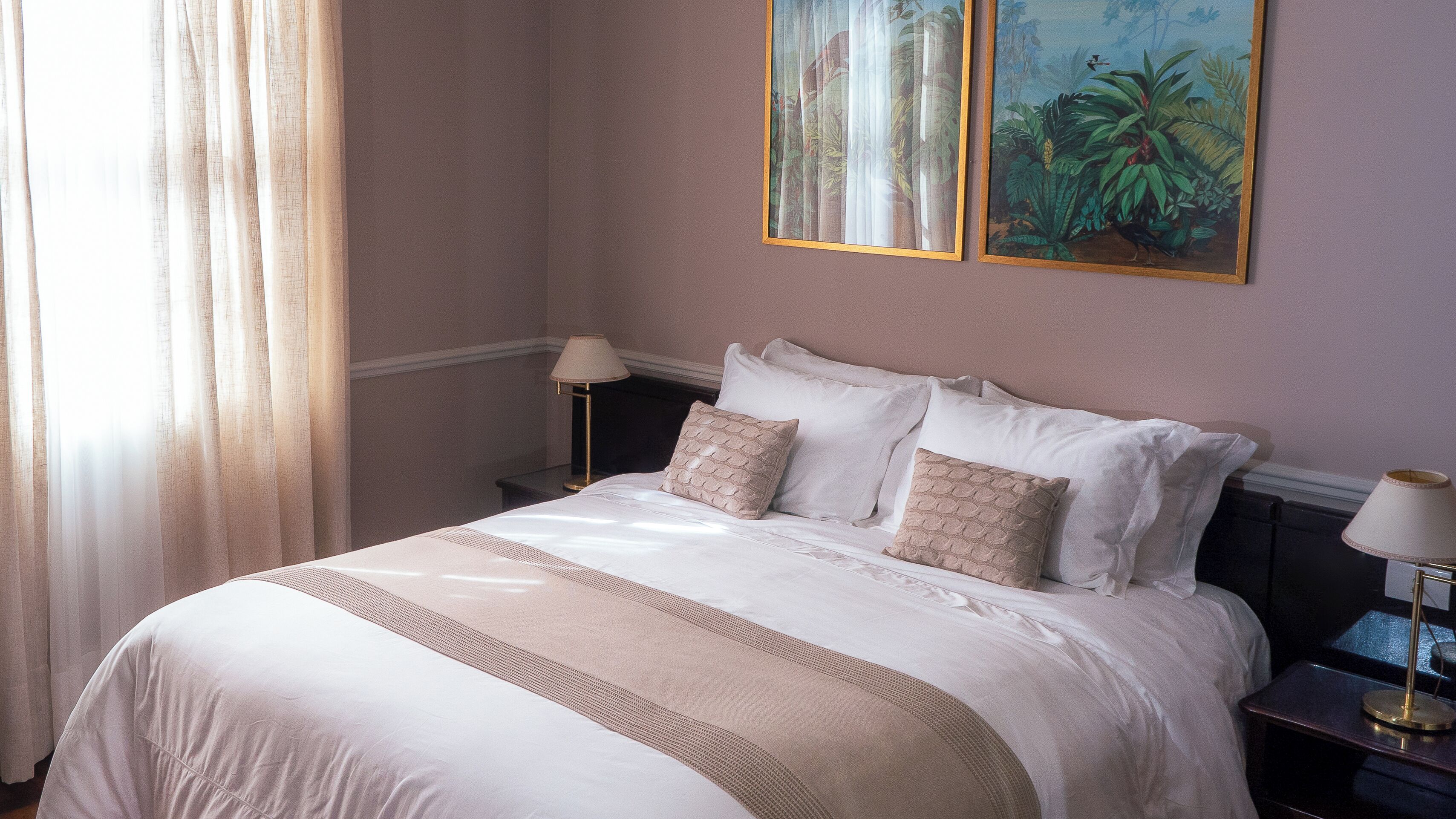 A neatly made bed with a white and beige bedspread, two pillows, and a nightstand with a lamp.