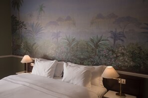 Una habitación de hotel con una cama, dos lámparas de noche y un mural de paisaje tropical en la pared.