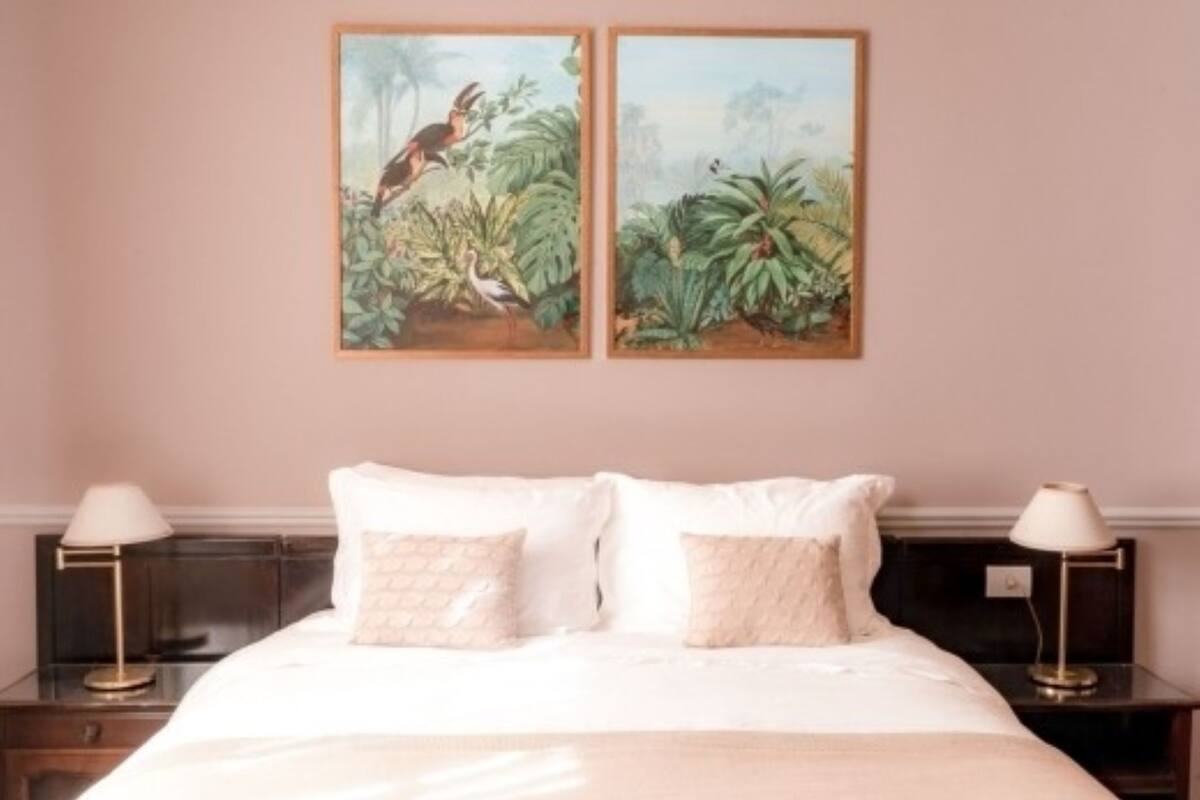 Quarto com uma cama, duas mesas de cabeceira e duas pinturas penduradas na parede retratando paisagens tropicais.