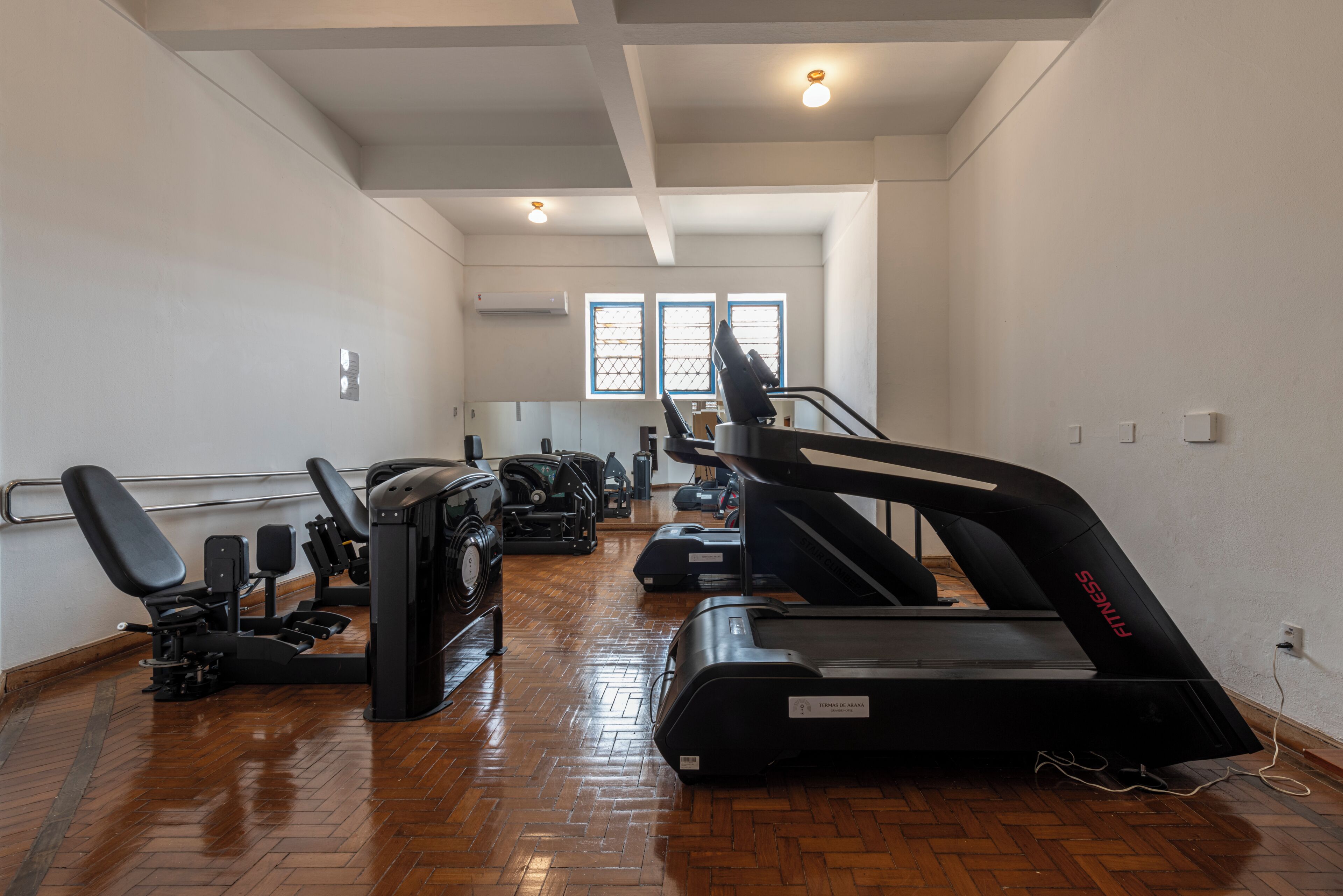 A gym with exercise equipment, wooden flooring, and a view of the outside through windows.