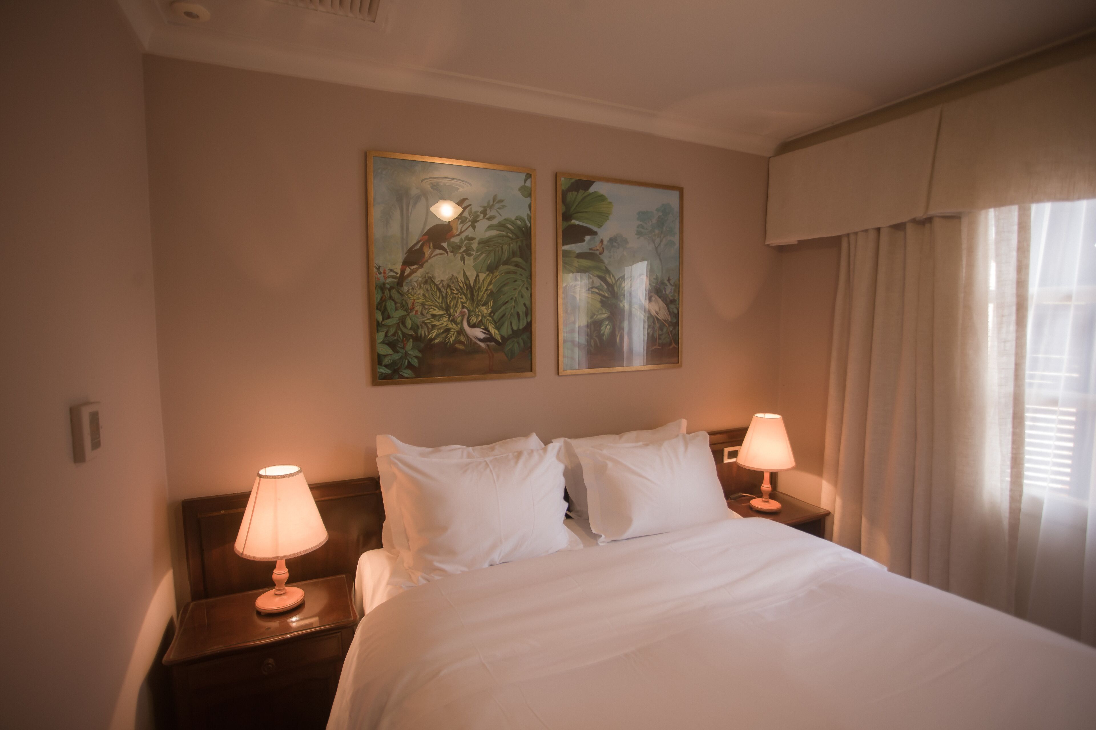 Quarto de hotel com uma cama grande, duas luminárias de cabeceira e duas pinturas emolduradas na parede.