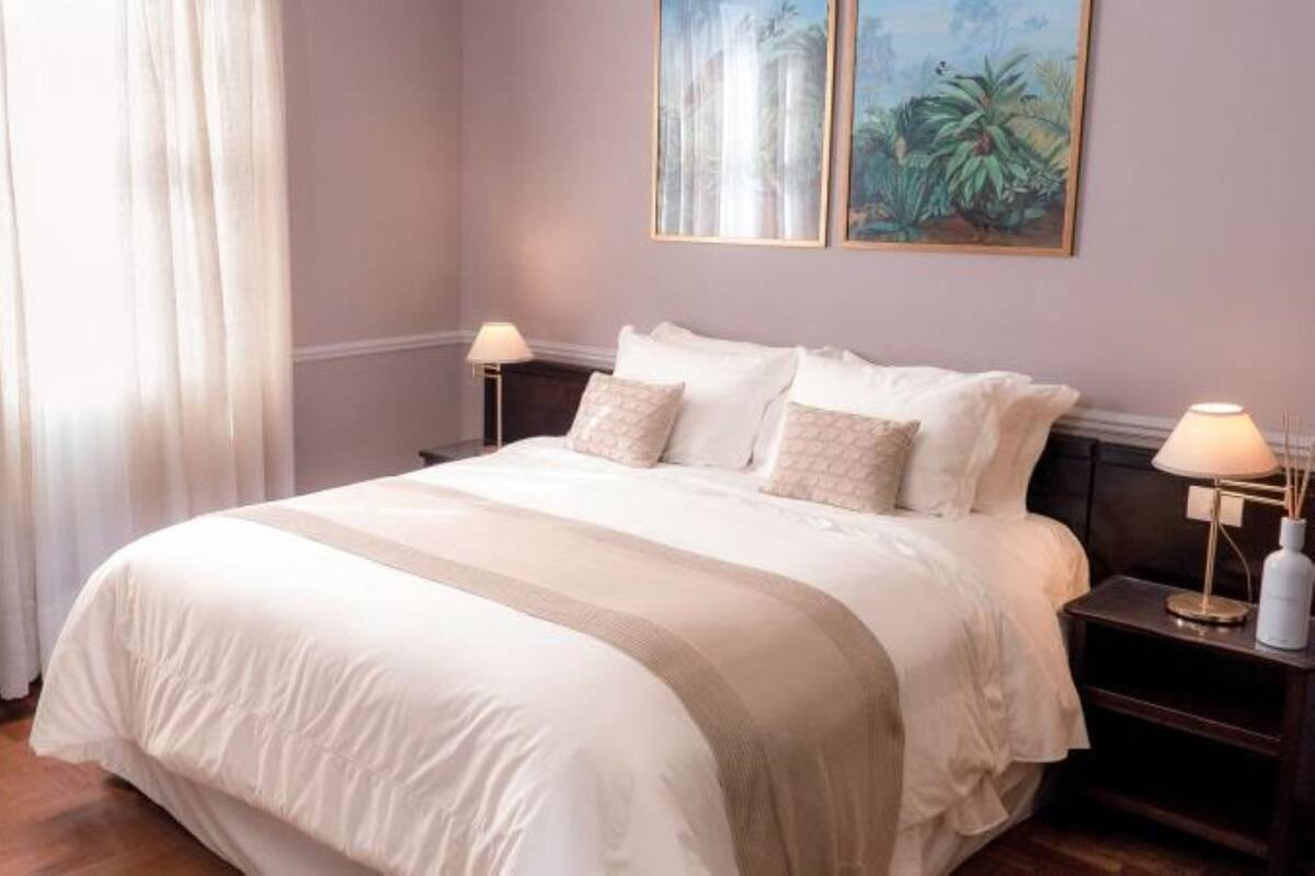 Uma cama bem arrumada com um edredom listrado, duas mesas de cabeceira com abajures e duas pinturas emolduradas na parede.