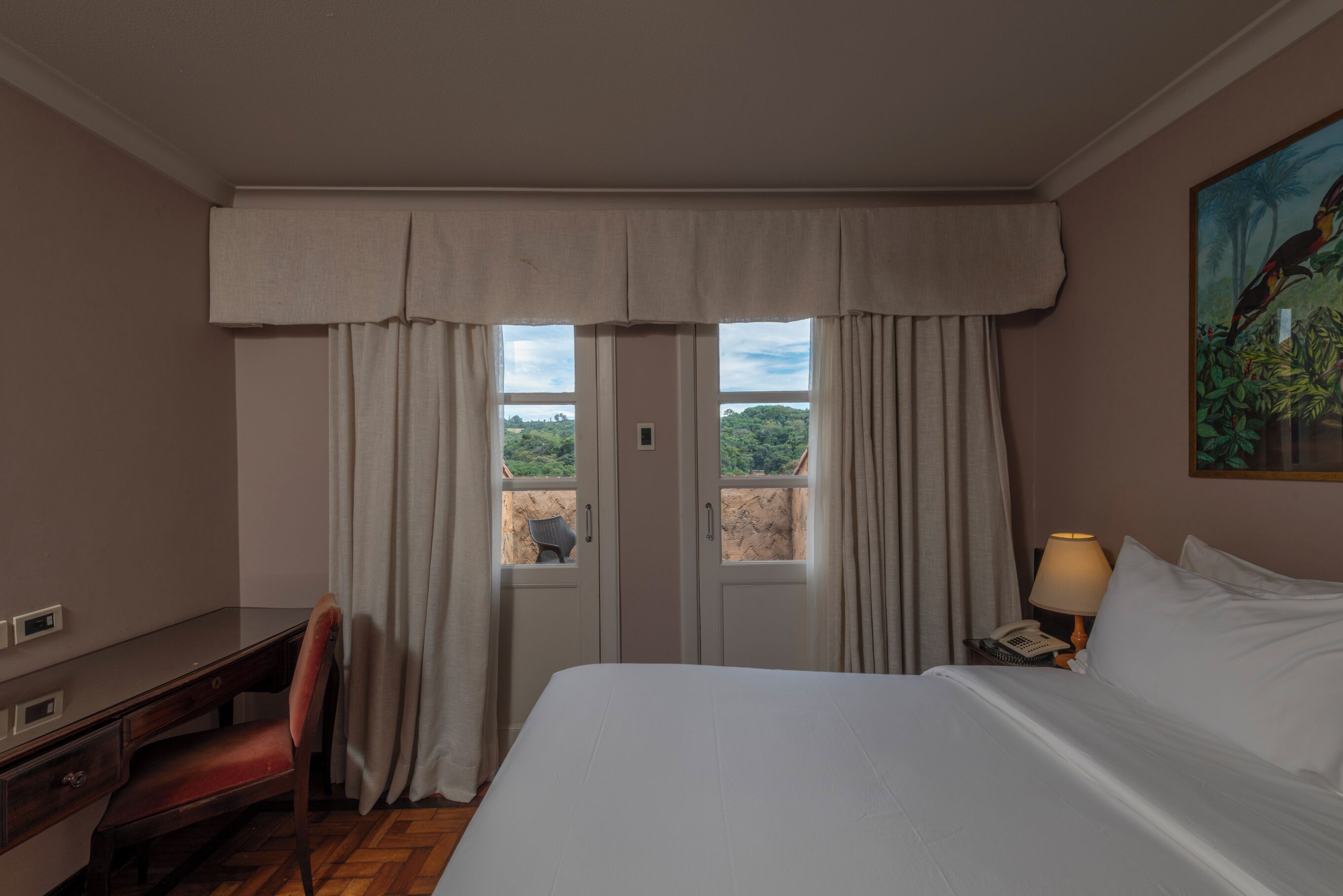 Een hotelkamer met een bed, een bureau, een stoel, een lamp en een schilderij.